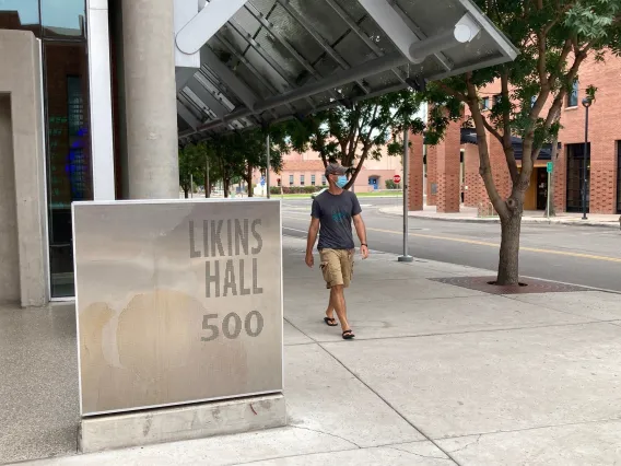 Photo of a man walking outside of the entrance to Likins Hall on the UA campus.