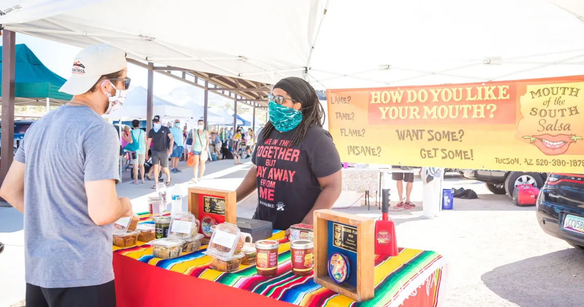 Person selling salsa to another person at a farmer's market