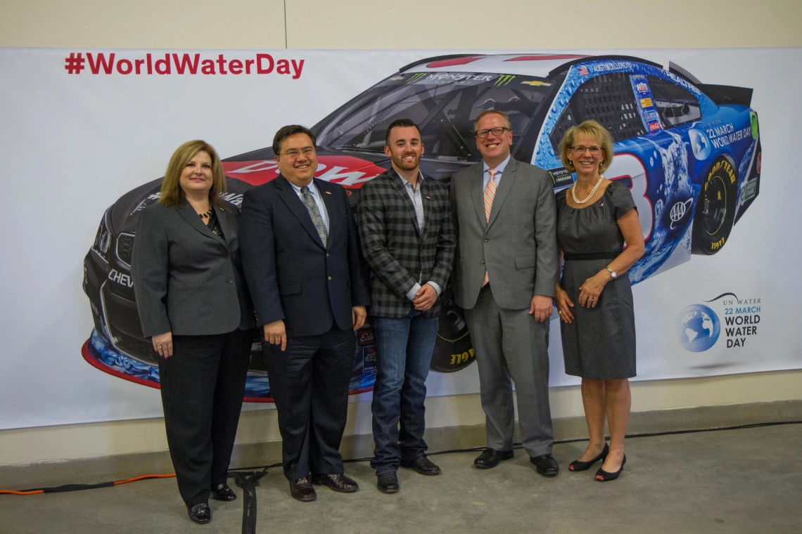 Group of people standing in front of World Water Day NASCAR poster.