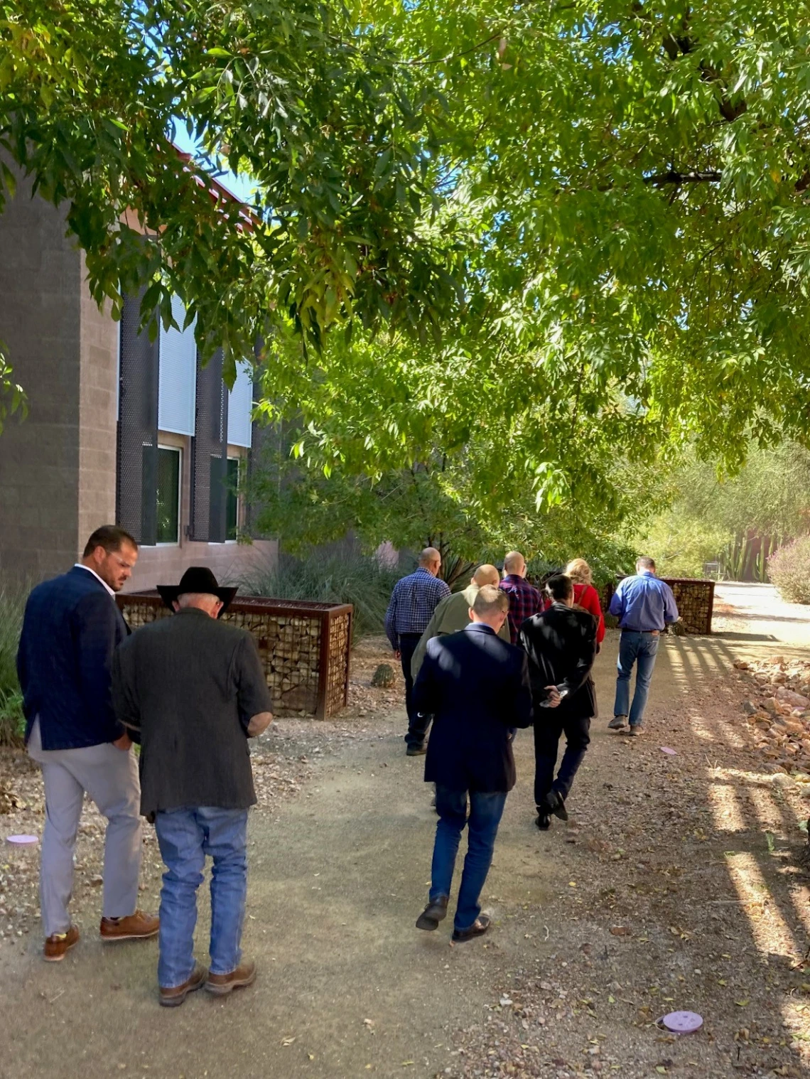 A group of people walk on a path with trees next to a building