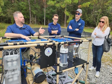 Four people standing by an outdoor water purification instrument.